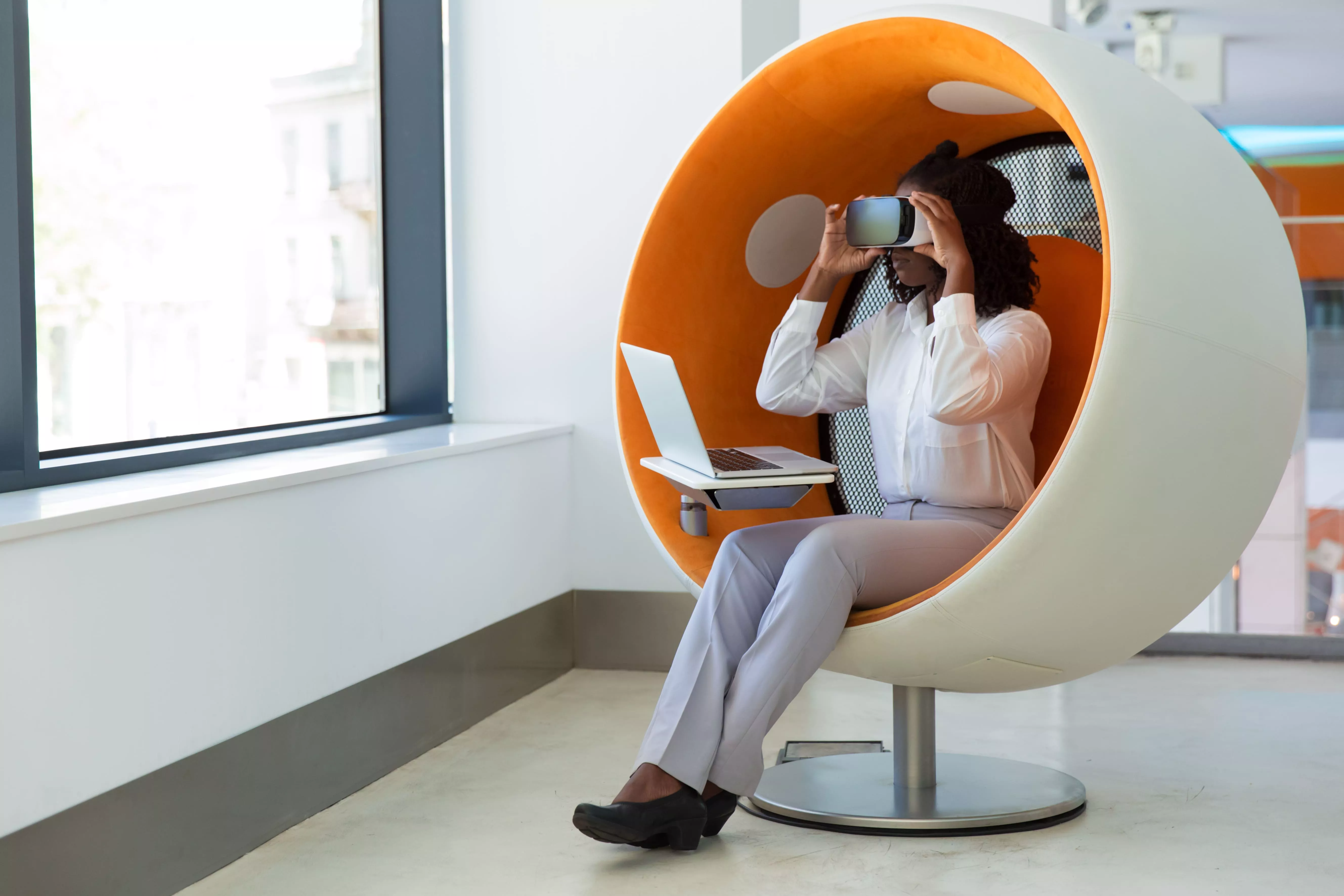 Une femme installée dans un fauteuil-cabine, casque de réalité virtuelle sur les yeux, un ordinateur portable ouvert à côté d’elle.