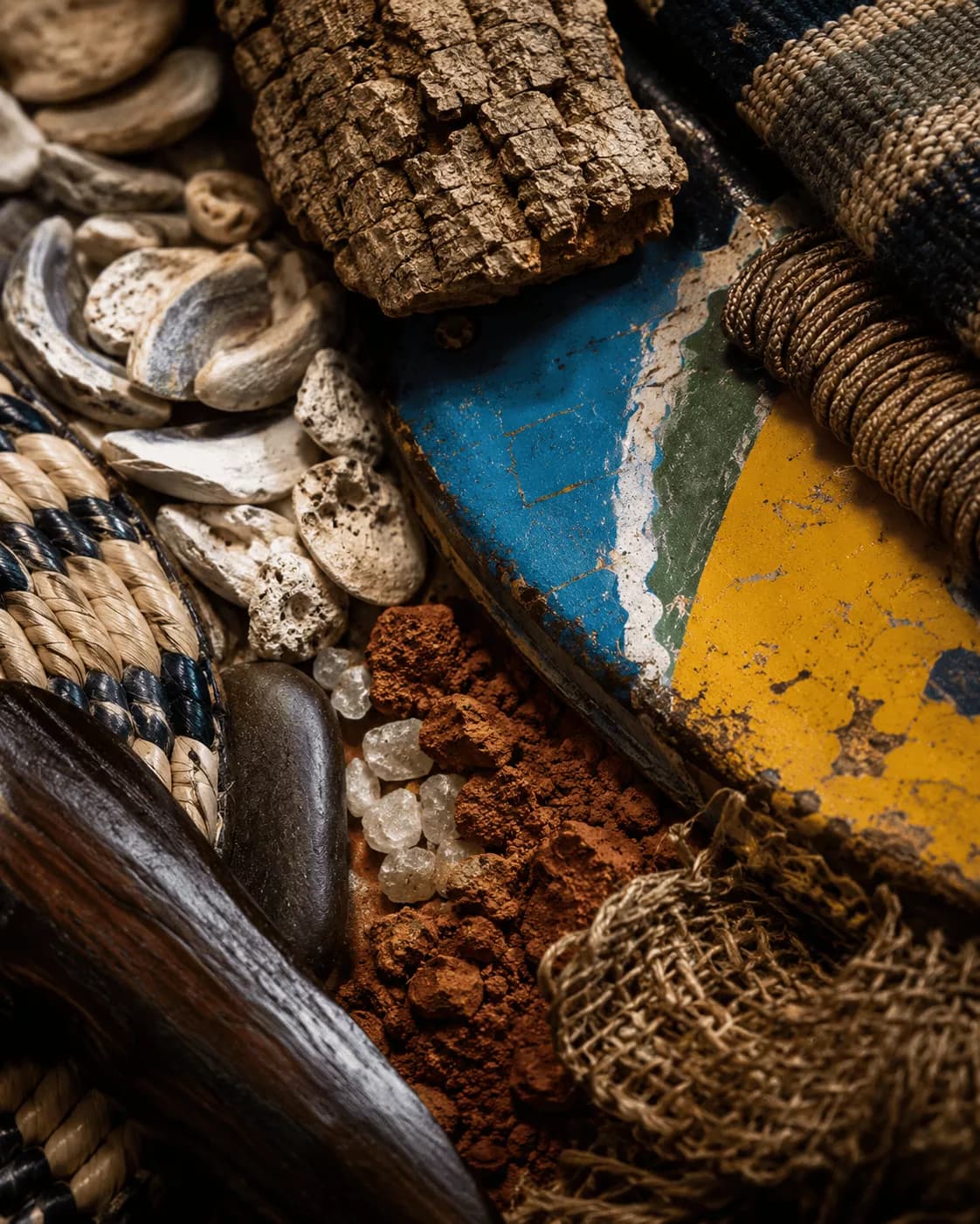 Un plan rapproché de matières assemblées : coquillages, écorce, vannerie, pigment de latérite, coque de pirogue peinte.